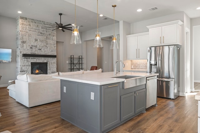 kitchen with gray cabinetry, stainless steel appliances, white cabinetry, a stone fireplace, and an island with sink