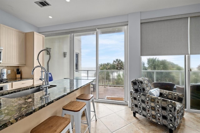 kitchen featuring a kitchen bar, backsplash, a wealth of natural light, and dark stone countertops