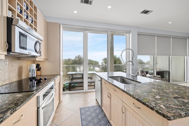 kitchen with sink, decorative backsplash, dark stone countertops, appliances with stainless steel finishes, and light tile patterned flooring