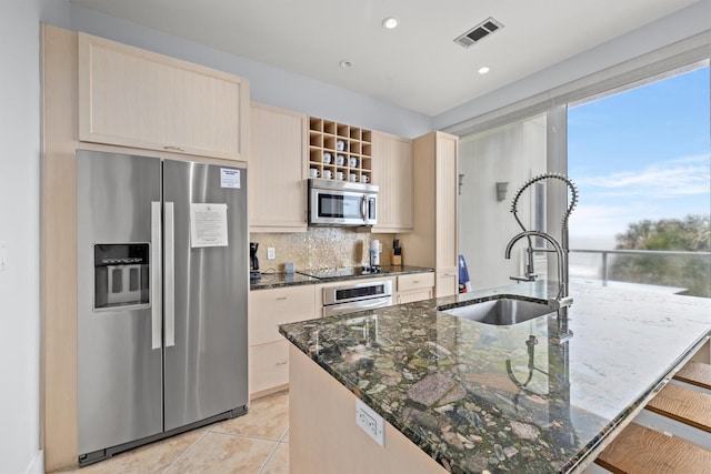 kitchen featuring sink, decorative backsplash, dark stone countertops, an island with sink, and appliances with stainless steel finishes