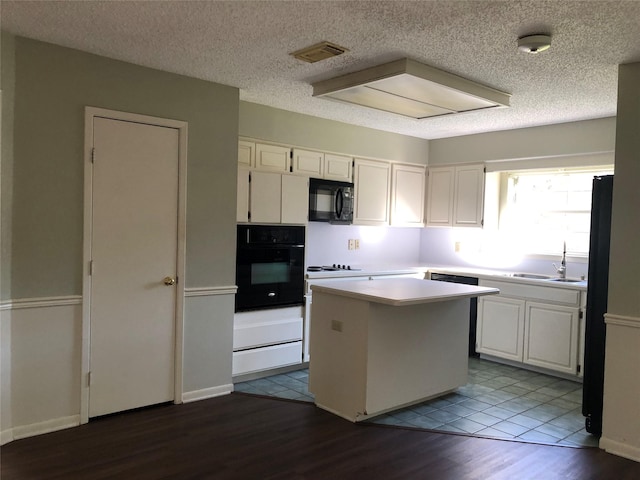 kitchen featuring sink, white cabinetry, a center island, black appliances, and a textured ceiling