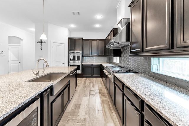 kitchen featuring stainless steel appliances, pendant lighting, dark brown cabinetry, and wall chimney range hood