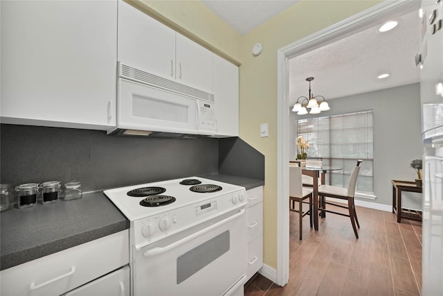 kitchen with a chandelier, wood-type flooring, white appliances, decorative light fixtures, and white cabinets