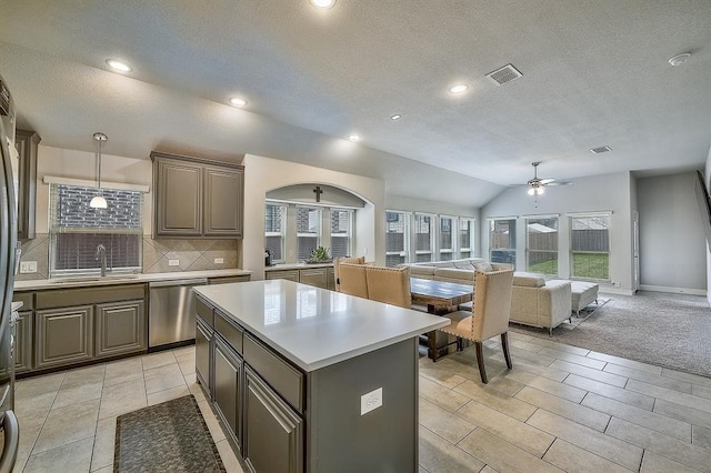 kitchen featuring pendant lighting, sink, vaulted ceiling, stainless steel dishwasher, and a kitchen island