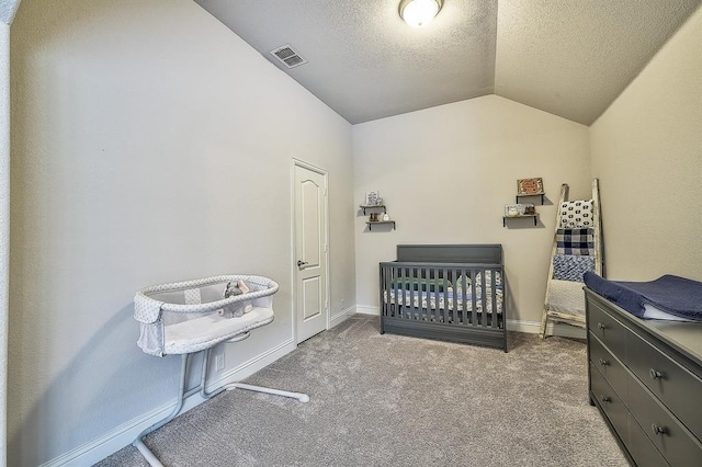 bedroom with a textured ceiling, a crib, light colored carpet, and lofted ceiling