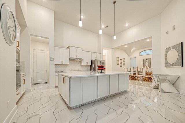 kitchen featuring a kitchen island with sink, high vaulted ceiling, white cabinets, hanging light fixtures, and decorative backsplash