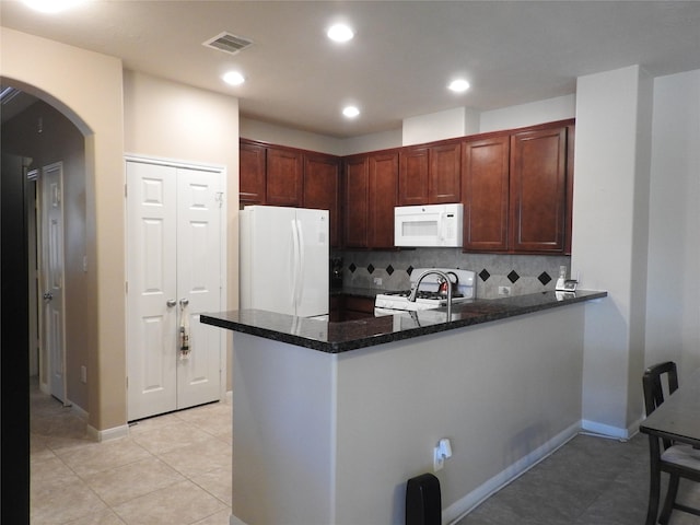 kitchen featuring kitchen peninsula, dark stone countertops, white appliances, decorative backsplash, and light tile patterned floors