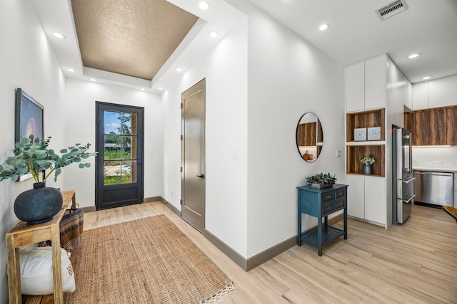 foyer entrance with a raised ceiling, light hardwood / wood-style flooring, and a textured ceiling