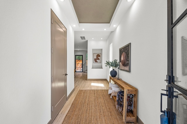 corridor with a raised ceiling and light hardwood / wood-style floors