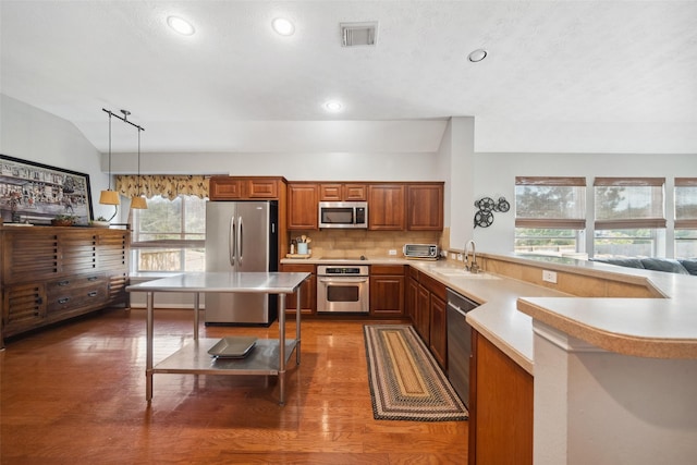 kitchen with sink, hanging light fixtures, decorative backsplash, appliances with stainless steel finishes, and kitchen peninsula