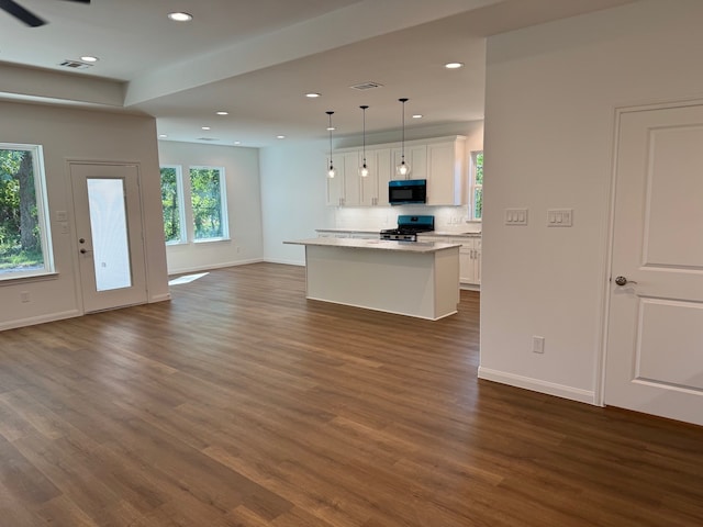 kitchen with dark hardwood / wood-style flooring, black gas range oven, pendant lighting, white cabinets, and a center island