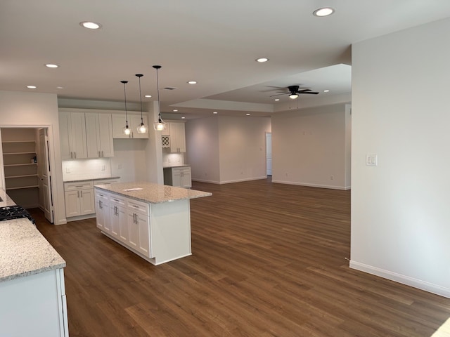 kitchen with white cabinetry, a center island, light stone counters, and decorative light fixtures