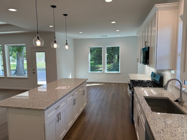 kitchen with stainless steel gas range oven, white cabinets, sink, a kitchen island, and light stone counters