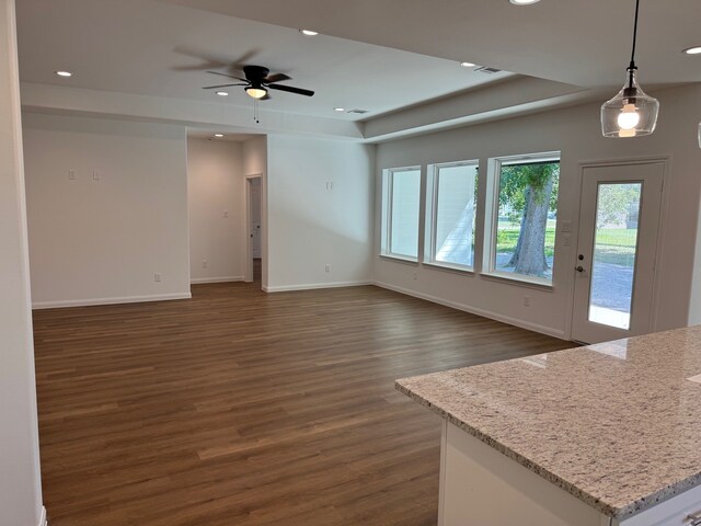 unfurnished living room with a tray ceiling, ceiling fan, and dark wood-type flooring