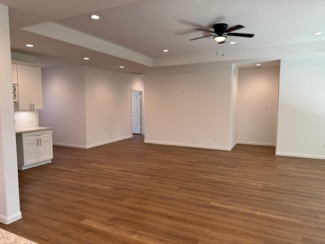 unfurnished living room with a raised ceiling, dark wood-type flooring, and ceiling fan