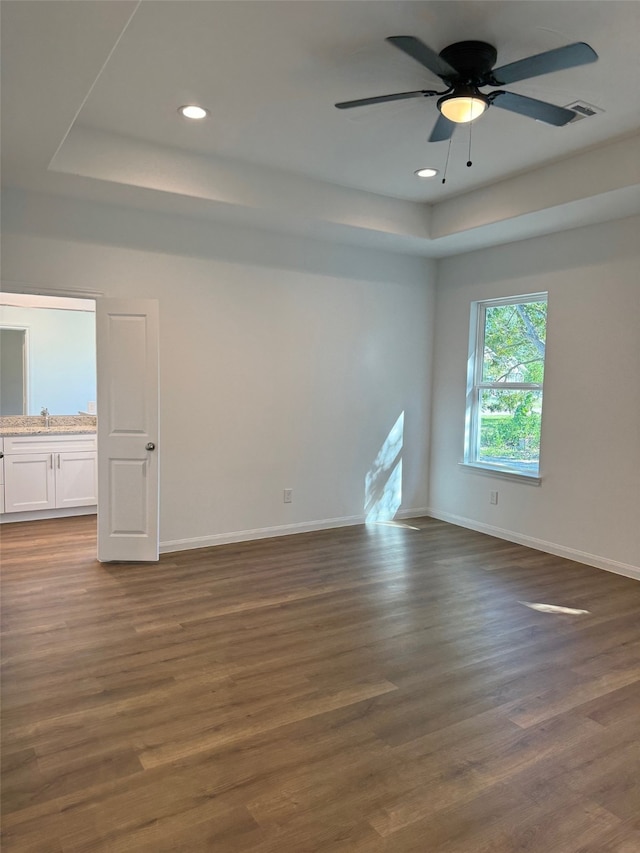 empty room with a tray ceiling, ceiling fan, and dark hardwood / wood-style floors