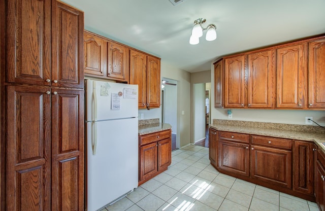 kitchen featuring white fridge, light stone counters, and light tile patterned floors