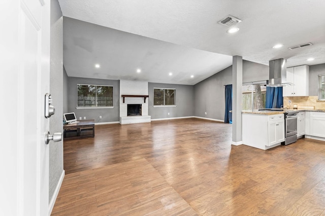 kitchen with white cabinetry, lofted ceiling, stainless steel range with electric stovetop, island range hood, and hardwood / wood-style flooring