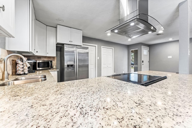 kitchen featuring light stone countertops, stainless steel appliances, island range hood, sink, and white cabinetry