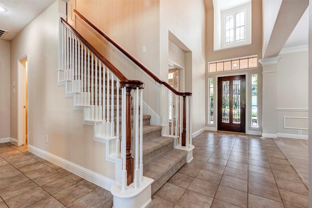 entrance foyer featuring light tile patterned floors, a towering ceiling, and ornamental molding