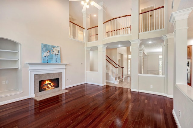 unfurnished living room with hardwood / wood-style floors, built in features, a high ceiling, and a tiled fireplace