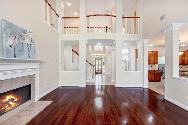 unfurnished living room with a tiled fireplace, a towering ceiling, and dark hardwood / wood-style floors