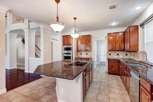 kitchen with dark stone counters, ornate columns, appliances with stainless steel finishes, a kitchen island, and a kitchen bar