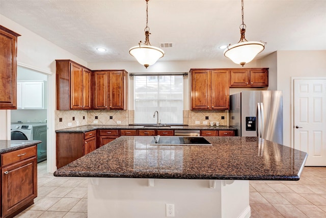 kitchen with a kitchen breakfast bar, sink, washer and dryer, stainless steel fridge, and an island with sink