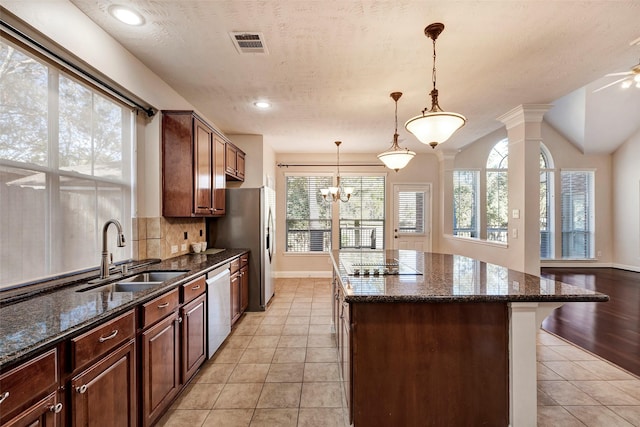 kitchen with sink, dark stone countertops, ornate columns, decorative light fixtures, and stainless steel appliances