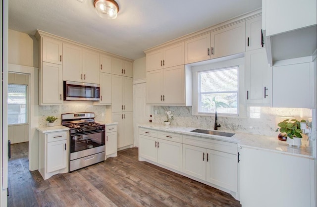 kitchen featuring dark hardwood / wood-style flooring, tasteful backsplash, light stone counters, stainless steel appliances, and sink