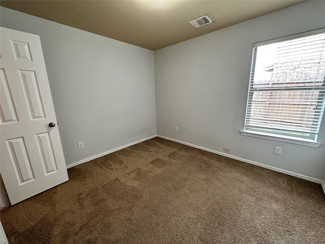 spare room with a wealth of natural light and dark colored carpet