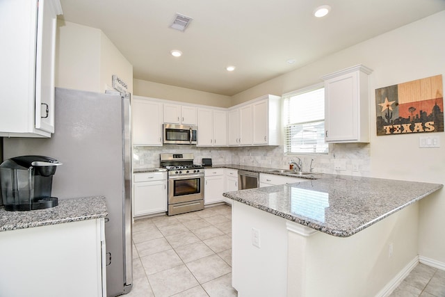 kitchen featuring kitchen peninsula, light stone counters, stainless steel appliances, sink, and white cabinets