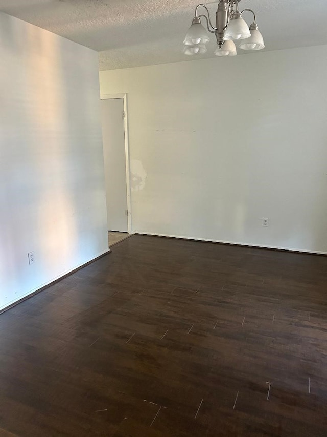 empty room featuring dark hardwood / wood-style flooring, a textured ceiling, and an inviting chandelier