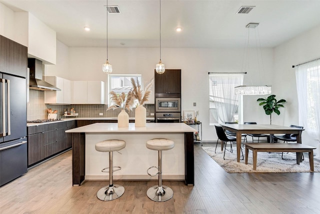 kitchen with pendant lighting, a center island, wall chimney exhaust hood, dark brown cabinets, and white cabinetry