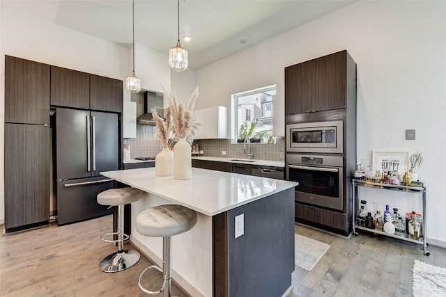 kitchen featuring light hardwood / wood-style flooring, wall chimney exhaust hood, a kitchen bar, dark brown cabinetry, and stainless steel appliances