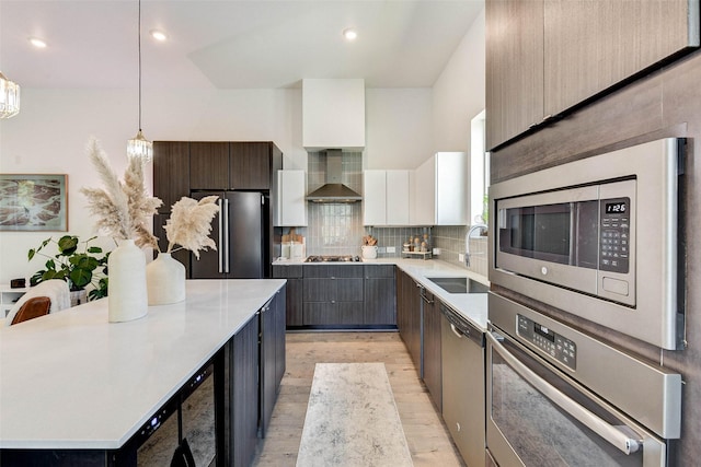 kitchen with sink, hanging light fixtures, wall chimney exhaust hood, white cabinetry, and stainless steel appliances