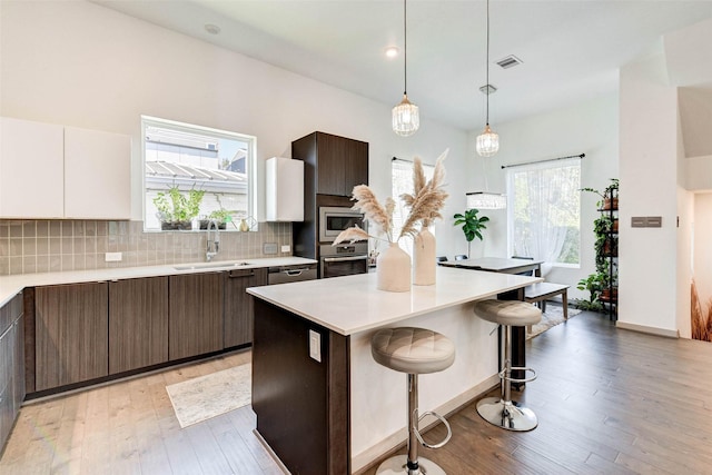 kitchen featuring appliances with stainless steel finishes, dark brown cabinets, sink, white cabinets, and a center island