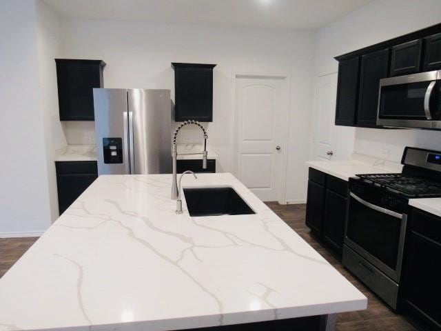 kitchen featuring dark wood-type flooring, sink, light stone countertops, an island with sink, and stainless steel appliances