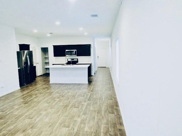 kitchen featuring a kitchen island with sink, sink, light wood-type flooring, and appliances with stainless steel finishes