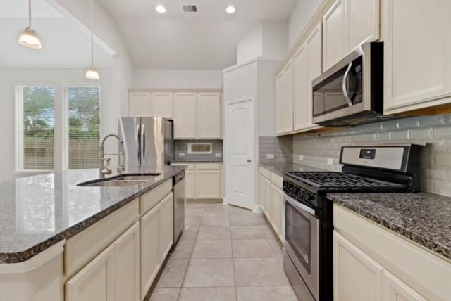 kitchen featuring a kitchen island with sink, hanging light fixtures, sink, decorative backsplash, and appliances with stainless steel finishes