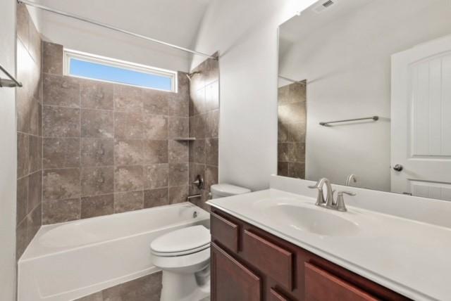 full bathroom featuring vanity, tiled shower / bath combo, and toilet