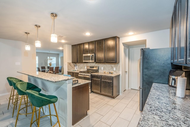 kitchen featuring tasteful backsplash, an island with sink, decorative light fixtures, a breakfast bar, and appliances with stainless steel finishes