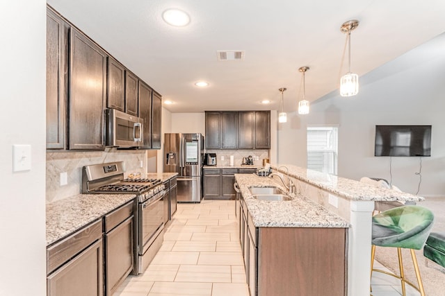 kitchen featuring dark brown cabinetry, sink, a kitchen breakfast bar, decorative light fixtures, and appliances with stainless steel finishes