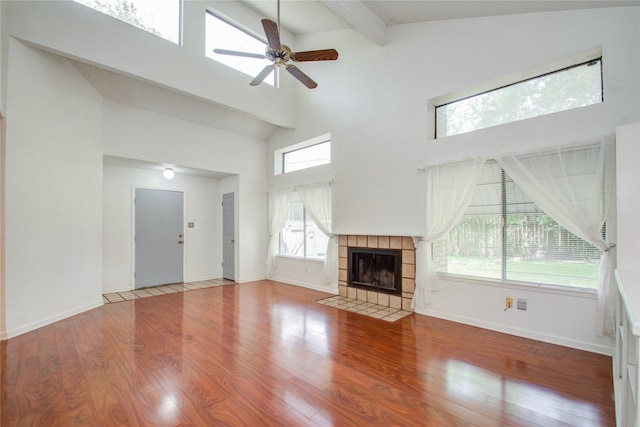 unfurnished living room featuring hardwood / wood-style floors, a tile fireplace, high vaulted ceiling, ceiling fan, and beamed ceiling