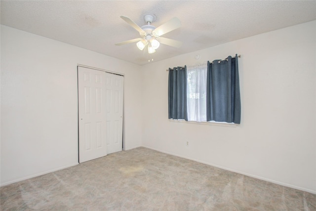 unfurnished bedroom featuring light carpet, a textured ceiling, a closet, and ceiling fan