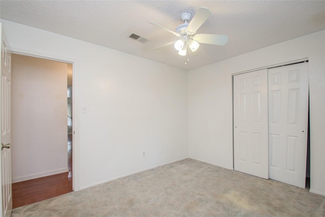 unfurnished bedroom with ceiling fan, a closet, light colored carpet, and a textured ceiling