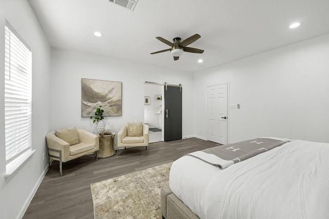 bedroom with a barn door, ceiling fan, dark hardwood / wood-style flooring, and multiple windows