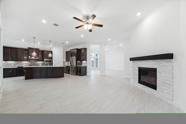 kitchen featuring pendant lighting, a center island with sink, ceiling fan, a fireplace, and stainless steel appliances