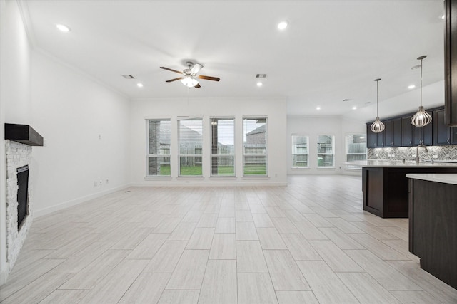 unfurnished living room with sink, crown molding, ceiling fan, light wood-type flooring, and a fireplace