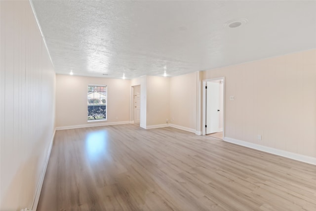 empty room with wood walls, a textured ceiling, and light hardwood / wood-style flooring